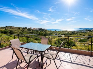 A terrace with a table and chairs, overlooking a hilly landscape with buildings in the distance.
