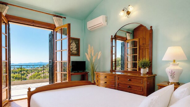 Une chambre avec un grand lit, une commode en bois, une télévision et une vue sur la mer, grâce à des portes ouvertes.