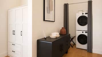 A room with a white wardrobe, a black cabinet with a vase and towels, and a wall-mounted washing machine.