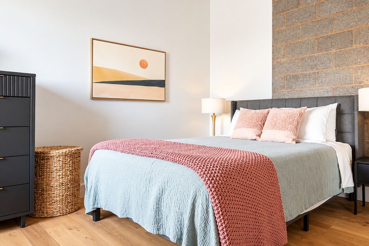 A bedroom with a bed, two bedside tables, a lamp, a picture on the wall, and a brick wall.