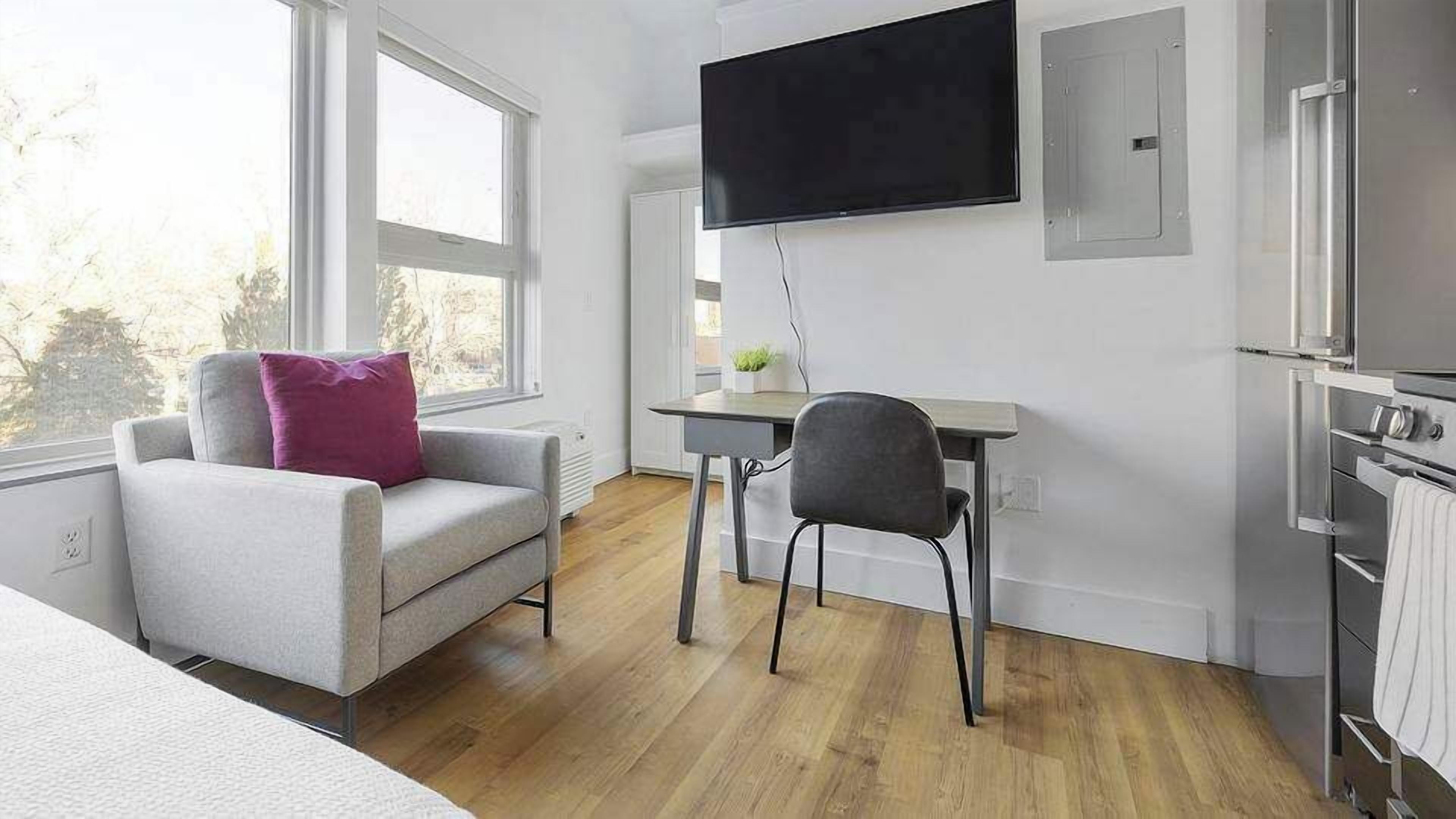 A modern room with a sofa, a chair, a flat-screen TV, a small table, and a built-in oven.