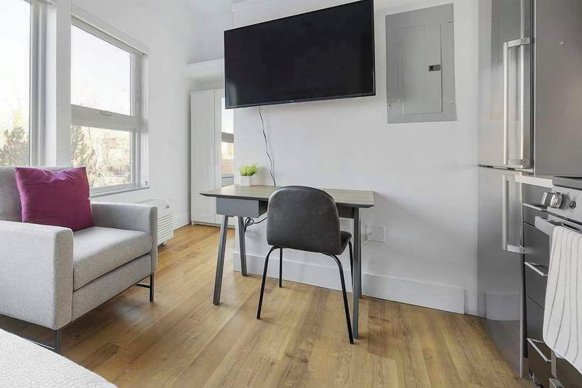 A modern room with a sofa, a chair, a flat-screen TV, a small table, and a built-in oven.