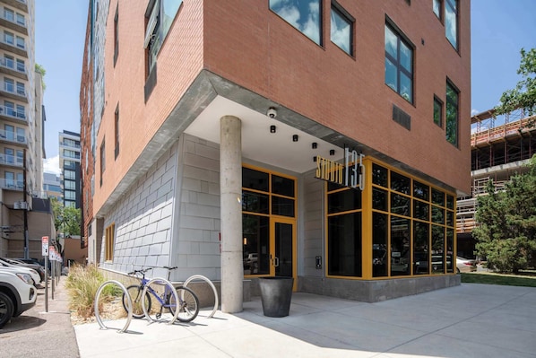 A modern building with a large glass entrance, a bike rack, and a parking area. - Roami at Studio 135 (Denver)