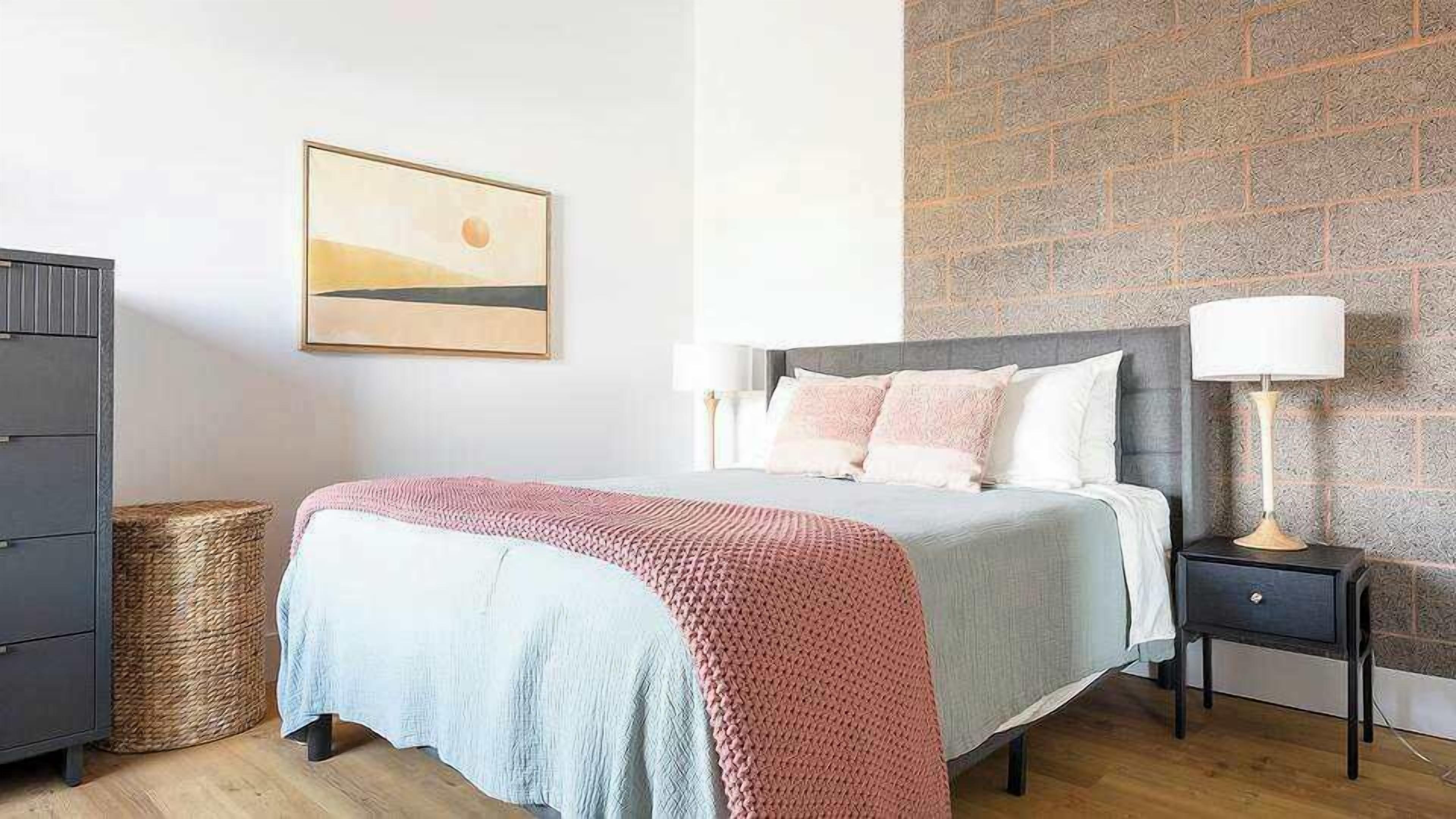 A bedroom with a bed, bedside tables, a lamp, a picture on the wall, and a wicker basket.