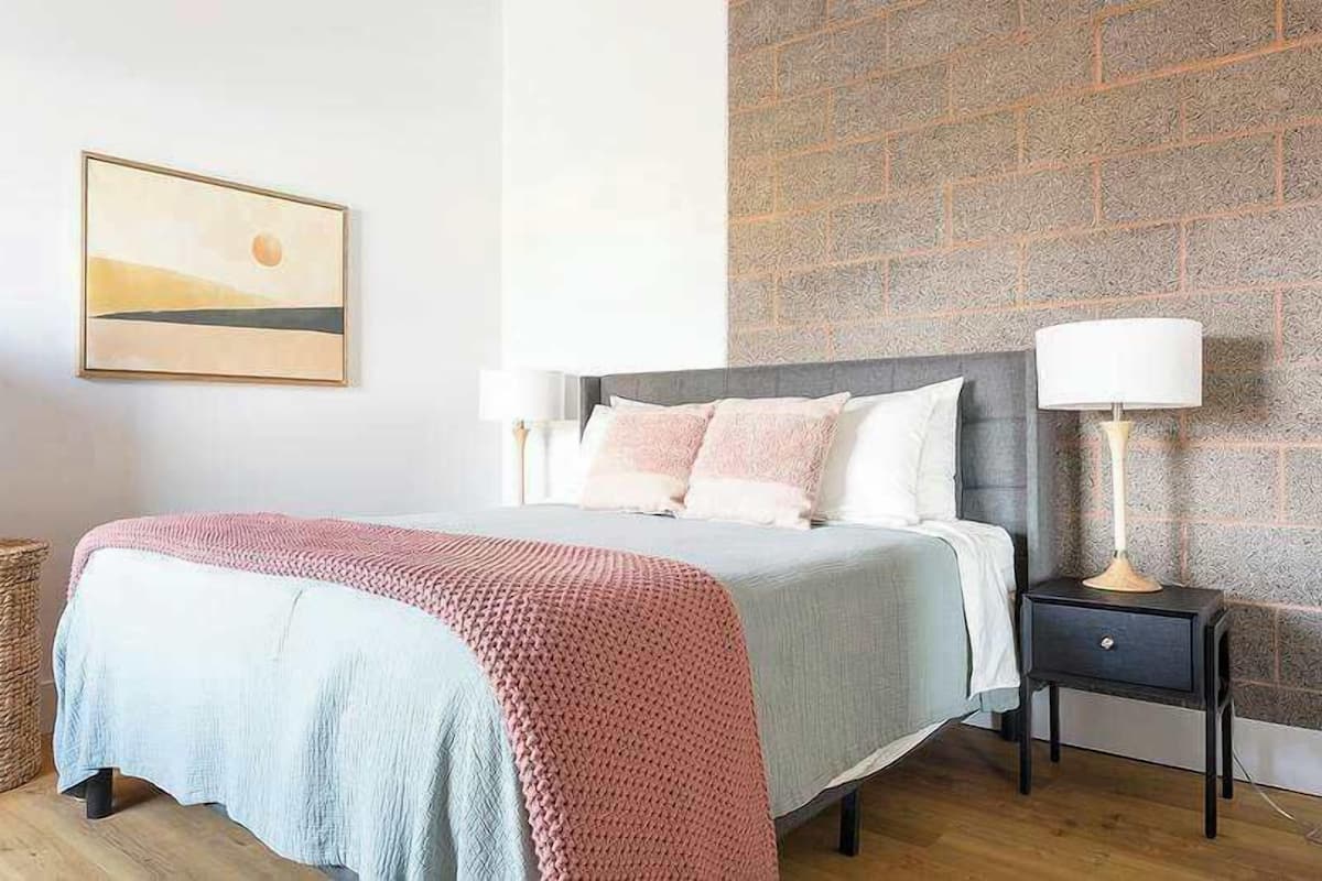 A bedroom with a bed, bedside tables, a lamp, a picture on the wall, and a wicker basket.