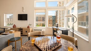 A modern living room with a chessboard, a TV, and a large window with a city view. - Roami at Studio 135 (Denver)