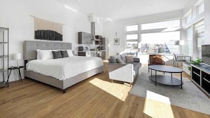 A modern bedroom with a large bed, a sofa, a dining table, and a kitchen area. - Roami at Studio 135 (Denver)