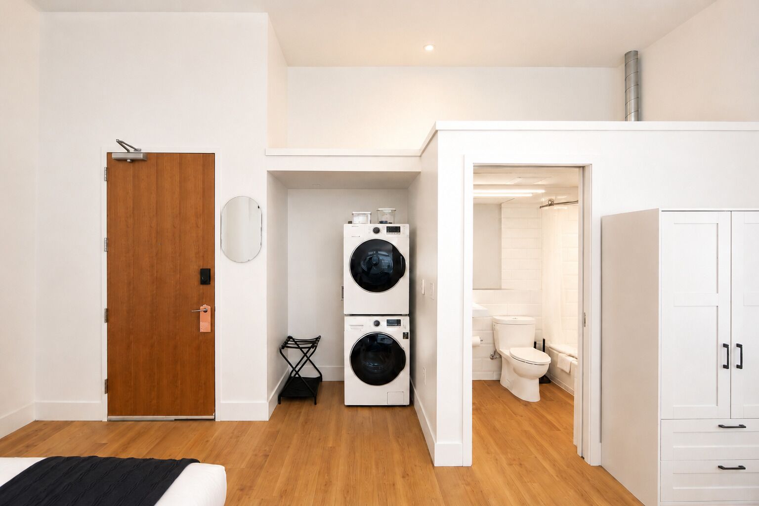 Un apartamento moderno con puerta de madera, un área de lavandería con dos lavadoras, un inodoro blanco y un armario blanco.