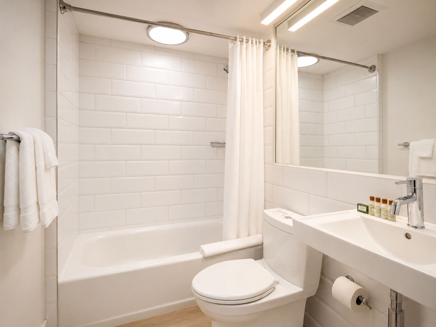 Un baño moderno con baldosas blancas, una bañera, un inodoro, un lavabo y un espejo.