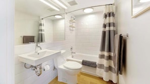 A modern bathroom with a white sink, toilet, and bathtub, a shower curtain, and a mirror. - Roami at Studio 135 (Denver)