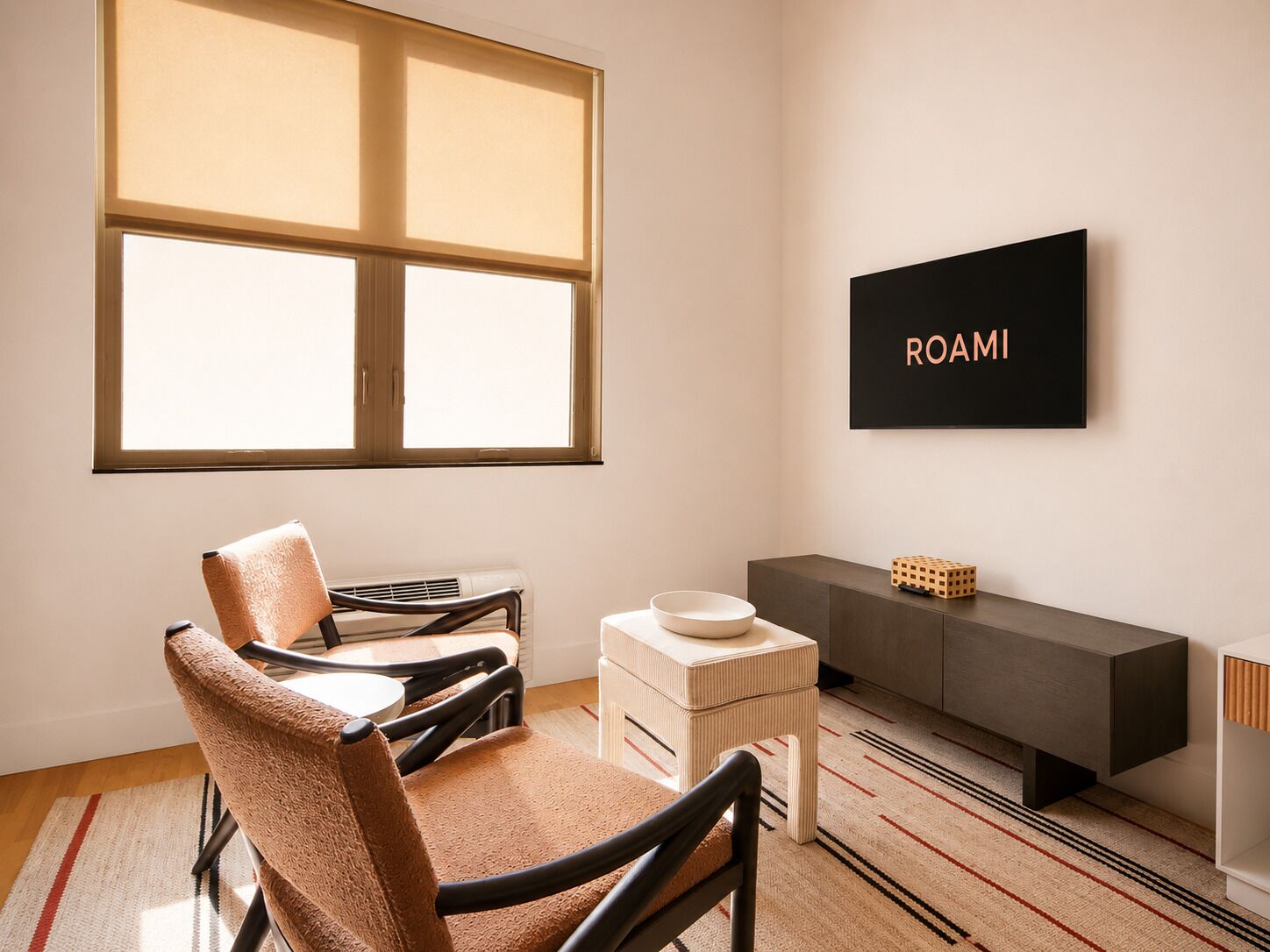 A modern room with a large window, a sofa, a small table, a cabinet, and a wall-mounted TV displaying 'ROAMI'.