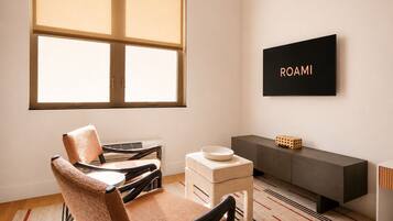 A modern room with a large window, a sofa, a small table, a cabinet, and a wall-mounted TV displaying 'ROAMI'.