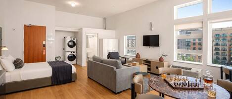 A modern apartment with a living area, a dining table with chess, a sofa, a TV, and a laundry room.