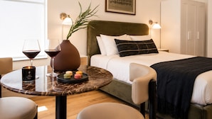 A hotel room with a bed, bedside lamps, a table with a candle, wine glasses, and a vase with a plant. - Roami at Studio 135 (Denver)