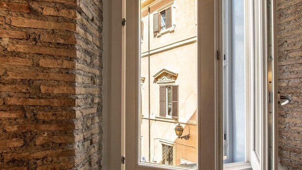 Blick durch eine Glastür in ein Gebäude, an einer Seite eine Ziegelwand und auf der anderen eine Fenster mit Rollläden.