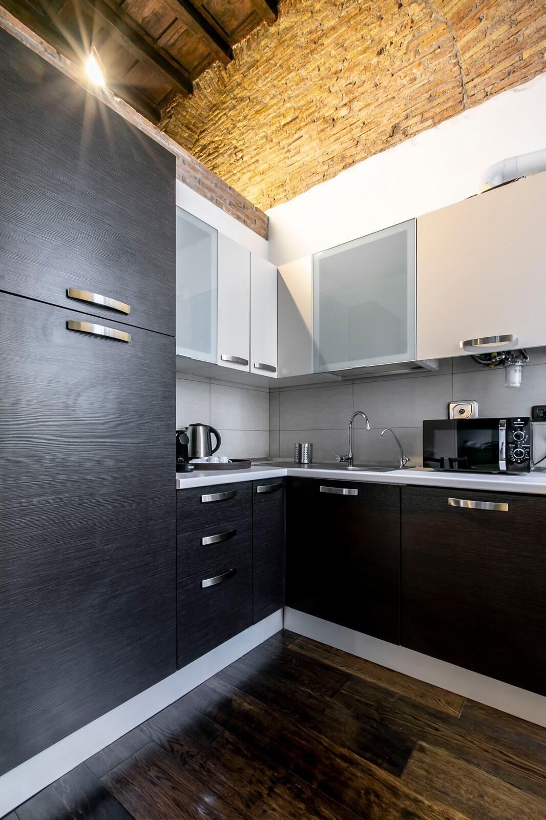 A modern kitchen with dark cabinetry, a stainless steel sink, and a microwave.