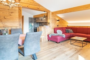 Ein gemütliches Zimmer mit Esstisch, Stühlen, einer roten Couch und einem kleinen Couchtisch.