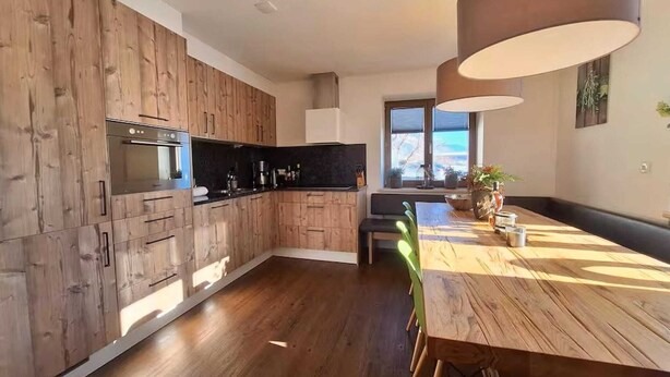 Eine moderne Küche mit Holzschränken, einem eingebauten Backofen und einem Essbereich mit Holztisch und -stühlen.