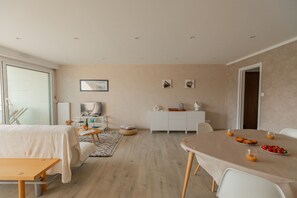 Ein modernes Hotelzimmer mit Essbereich, einem weißen Schrank, einem Fernseher und einem großen Fenster.