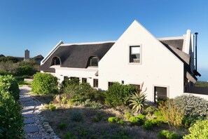 Une maison moderne avec un toit en pente, un chemin de pierre et une végétation luxuriante tout autour.