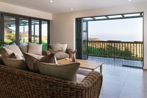 A modern living room with a large window, wicker furniture, and a view of the sea.
