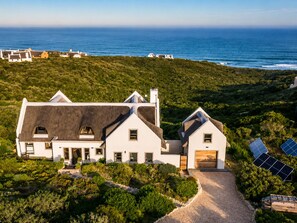 A modern house with a large driveway, solar panels, and a view of the ocean.
