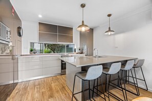 A modern kitchen with a large island, bar stools, pendant lighting, and a view of the outdoors. - Relaxed 2 Bed Coastal Stay Near the Lake (Buff Point)