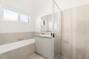 Un baño moderno con bañera, ducha con mampara de vidrio y tocador con espejo.
