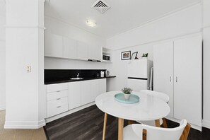 Eine moderne Küche mit weißen Schränken, einer schwarzen Arbeitsplatte, einem weißen Esstisch mit Stühlen und einem Blumentopf auf dem Tisch.