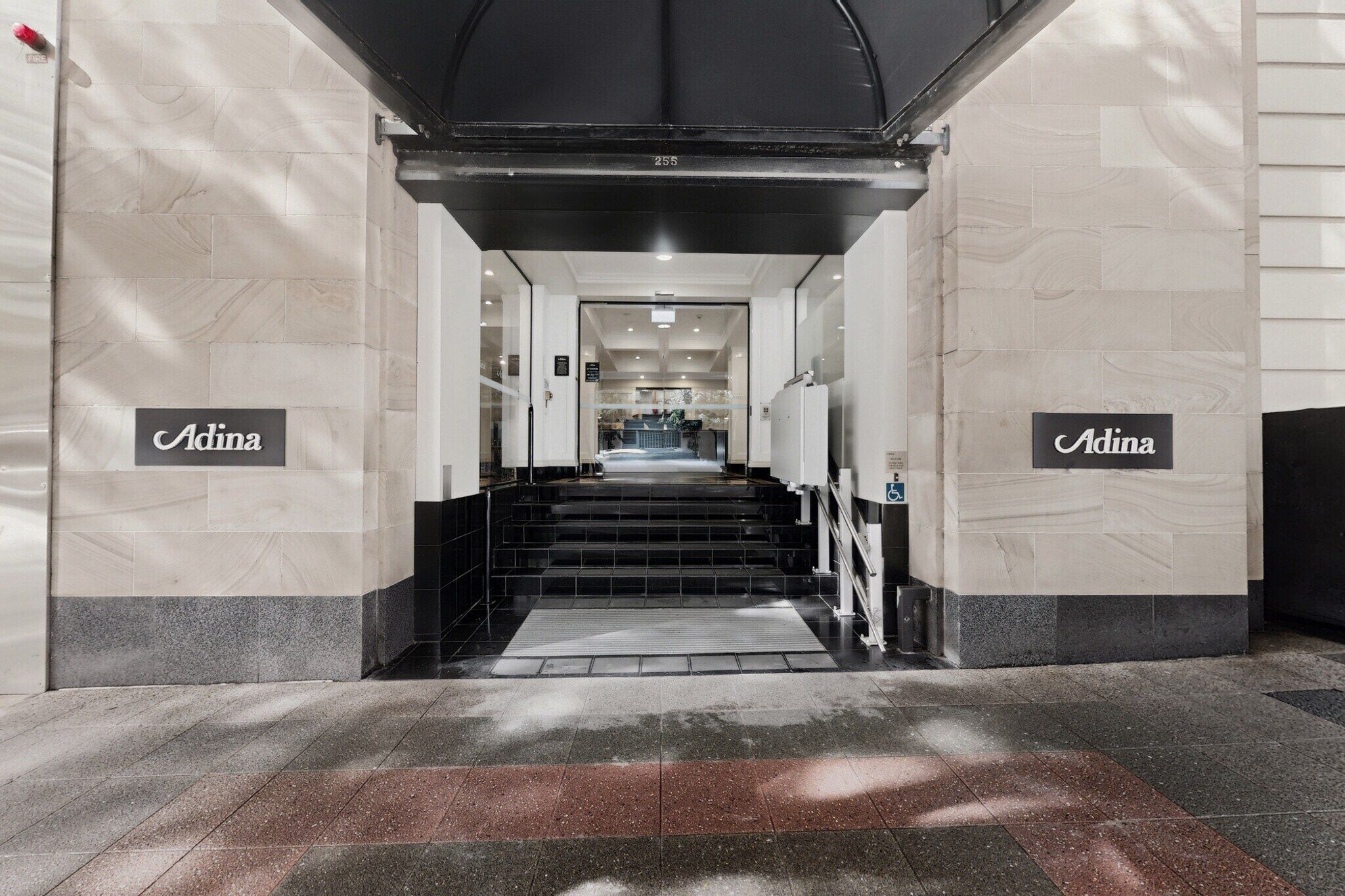 Ein Hotel Eingang mit einer Treppe zu einer Rezeption, gekennzeichnet durch 'Adina'-Schilder an beiden Seiten.