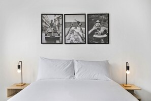 A bed with white bedding, two bedside tables with black lamps, and three black-and-white photographs on the wall. - Bright Apartment Near St Kilda Beachfront (Saint Kilda West)