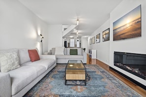 A modern living room with a sofa, coffee table, fireplace, and artwork on the walls. - Bright Apartment Near St Kilda Beachfront (Saint Kilda West)