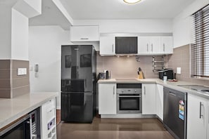 A modern kitchen with white cabinetry, a black refrigerator, an oven, and a dishwasher. - Bright Apartment Near St Kilda Beachfront (Saint Kilda West)