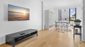 Ein modernes Wohnzimmer mit großem Flachbildfernseher, einer dunkelbraunen Unterhaltungsecke, einem Glastisch mit Stühlen und einem Bücherregal.