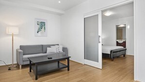Ein modernes Zimmer mit grauem Sofa, einem kleinen Tisch, einer Stehlampe und einer Schiebetür zu einem Badezimmer.