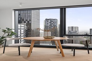 Ein modernes Zimmer mit großem Fenster, einem runden Holztisch, zwei Stühlen und einer Vase mit getrockneten Ästen.