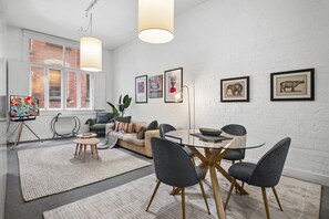 Ein modernes Wohnzimmer mit einer Couch, einem Glastisch, Stühlen, einem großen Fenster mit Blick und gerahmten Bildern an der Wand.