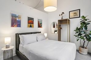 Ein ordentlich eingerichtetes Hotelzimmer mit Bett, Nachttischlampen, einem Spiegel, einer Ablage mit Dekoration und Wandbildern.