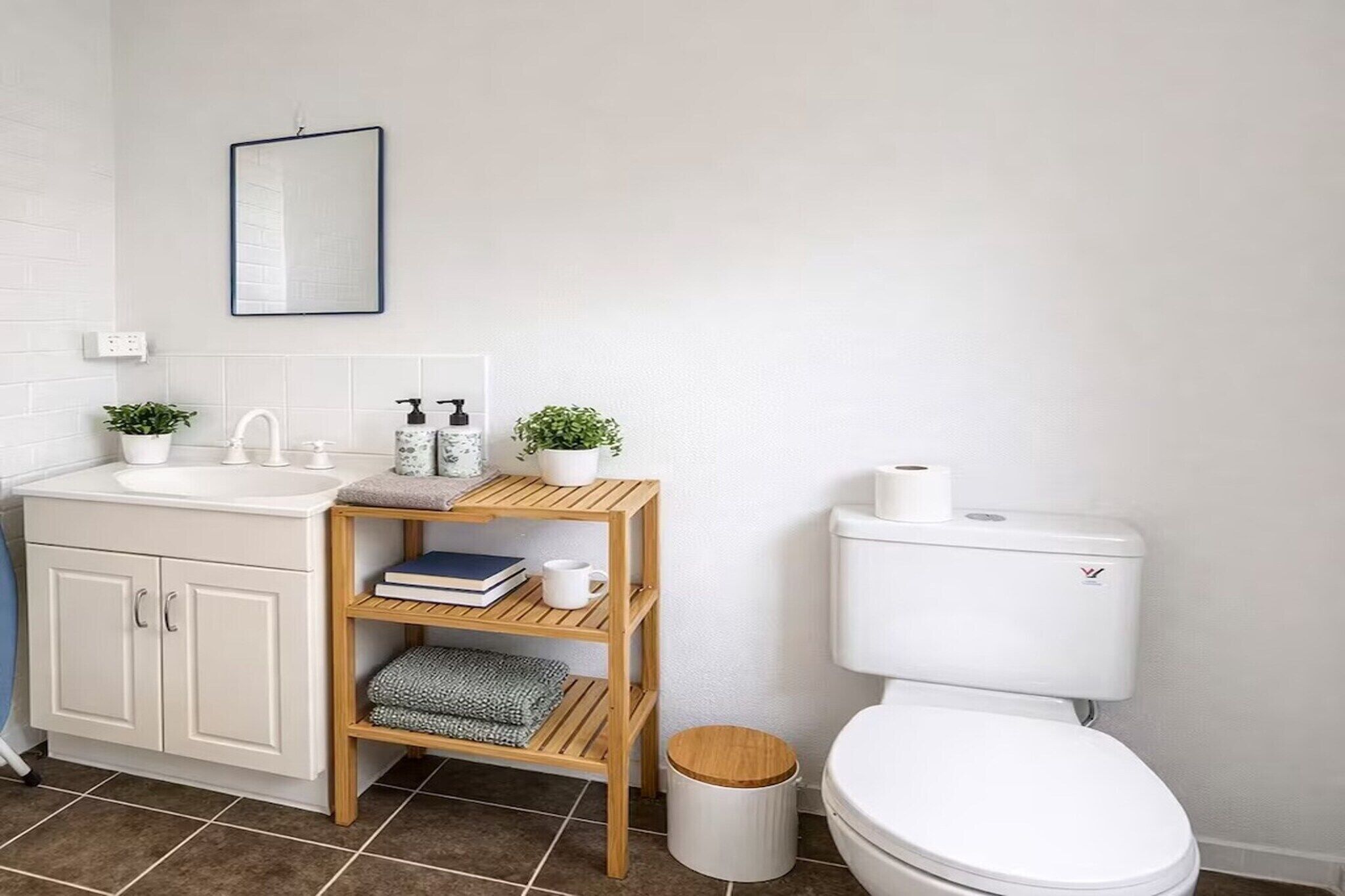 Un bagno con un lavandino bianco, un water e uno scaffale in legno con articoli da toilette.