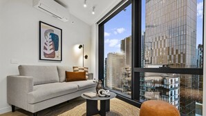 A modern living room with a sofa, a round coffee table, and a large window with a city view. - High-Rise 2-Bed Stay at Queensbridge (Southbank)