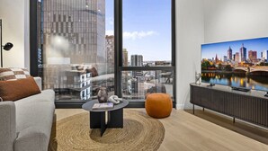 A modern living room with a large window, a sofa, a coffee table, and a cityscape painting. - High-Rise 2-Bed Stay at Queensbridge (Southbank)