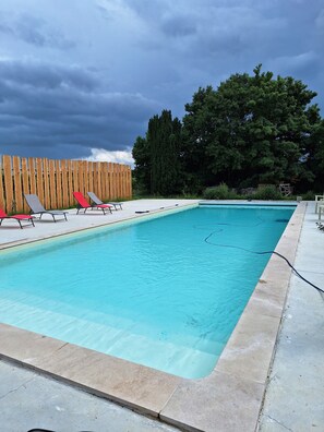 En rektangulär swimmingpool med ett trästaket och solstolar.