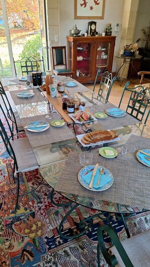 Una zona de menjador amb una taula llarga preparada per a dinar, rodejada de cadires.