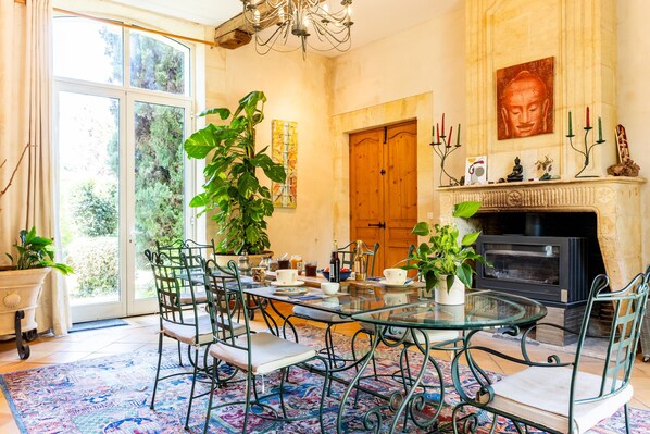 Un comedor con mesa de vidrio, sillas de metal, una planta grande en maceta y una chimenea con velas.