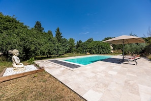 Una piscina con una estatua de Buda, un patio cubierto y vistas a un área boscosa.