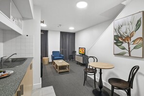 Ein kompaktes Hotelzimmer mit Küchenzeile, einem Essbereich mit Tisch und Stühlen sowie einer Sitzecke mit einer Couch und einem Fernseher.