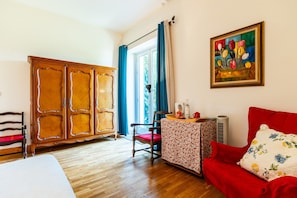 A room with a wooden wardrobe, a red sofa, a patterned table, and a painting on the wall.