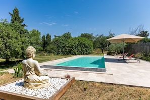 A swimming pool with a Buddha statue, a wooden deck, and a covered seating area.