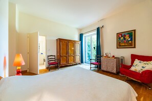 Una camera da letto con un letto, una poltrona rossa, un armadio in legno, un tavolo e un quadro appeso al muro.