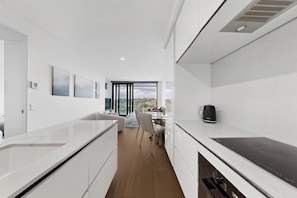 Una cocina moderna con armarios blancos, un comedor con mesa y sillas, y vistas a través de un ventanal.